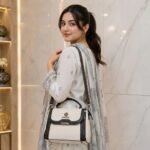 Young Pakistani woman wearing a white and gray embroidered lawn dress carrying the FOXJAZZ off-white shoulder bag.