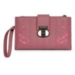 A muted dusty rose-pink faux leather women's long wallet or wristlet clutch. It displays parallel vertical stitching lines and symmetrical corner embroidery of intricate pink-on-pink floral rose patterns. Secure closure is provided by a distinctive metallic turn-lock featuring a smooth white insert. A practical wristlet strap is on the left side.